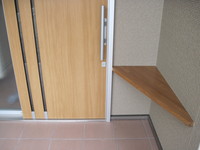 トステムの玄関引き戸エルムーブ＋簡易タッチキーシステムを採用。片手でも楽々解錠・施錠が可能で、片手で軽々と開られ、閉める時は自動的に。そして入口右に荷物置の棚を提案。
